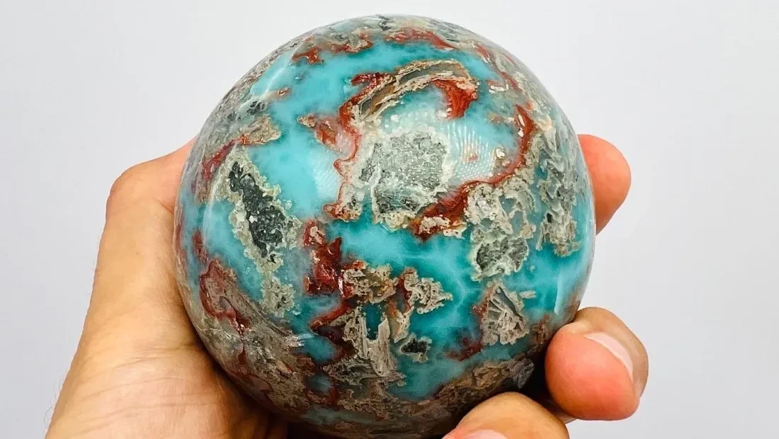 Hand holding a polished multicoloured Art Larimar specimen.