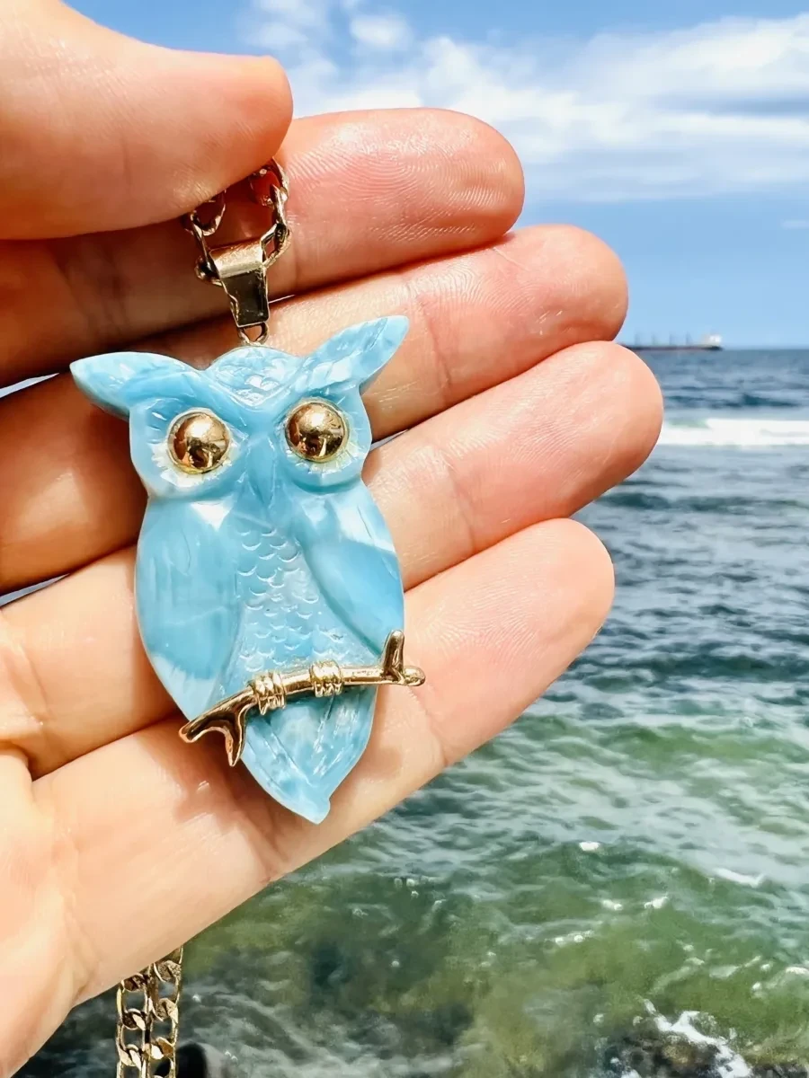 A Larimar owl pendant with metal details displayed in one hand.
