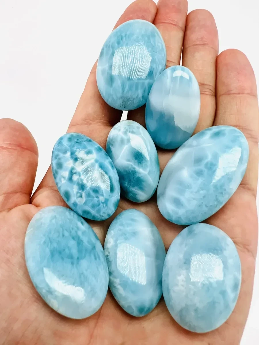 Several polished Larimar palm stones displayed in one hand.
