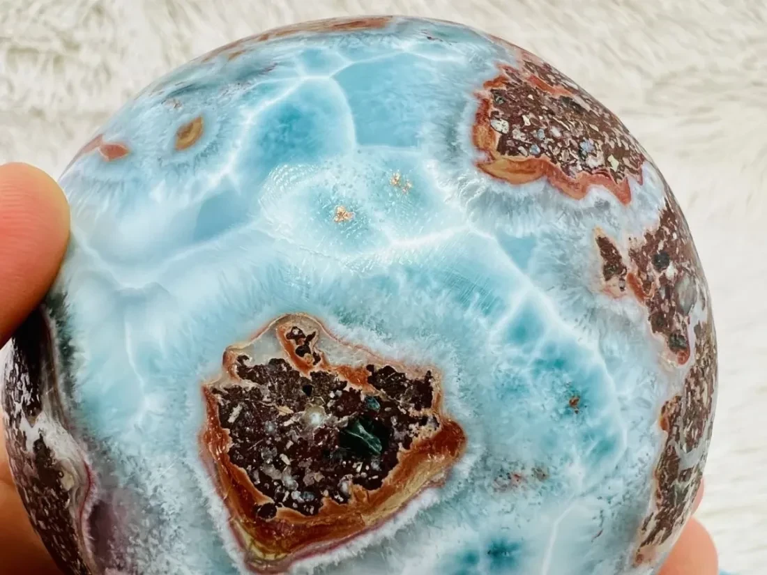 A polished Larimar sphere showing blue patterning and copper-coloured inclusions.