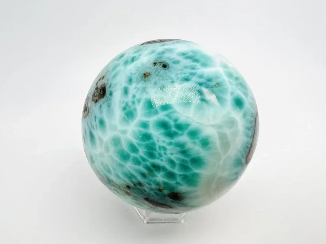 A polished Green Larimar sphere on a clear stand.